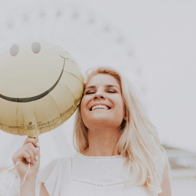 pexels-photo-1236678-1236678 Cheerful woman holding a smiley balloon outdoors on a sunny day, exuding happiness and positivity.